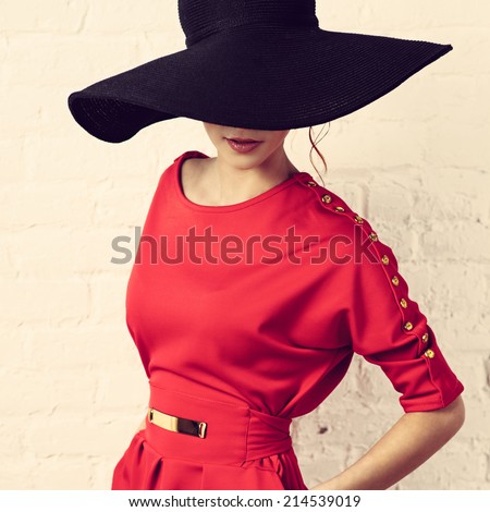 Beautiful young fashionable woman posing in red dress and black hat. Vogue style. Photo with instagram style filters