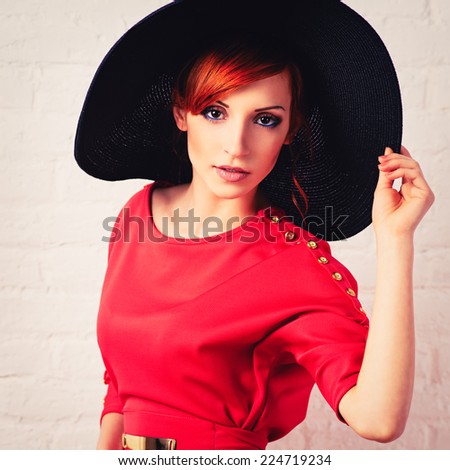 Beautiful young fashionable woman posing in red dress and black hat. Vogue style. Photo with instagram style filters