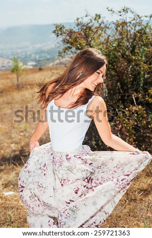Portrait of the young beautiful smiling woman outdoors enjoying summer sun. wind in hair. girl in a long skirt and with long hair poses in warm spring day