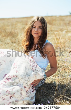 Portrait of the young beautiful smiling woman outdoors enjoying summer sun. wind in hair. girl in a long skirt and with long hair poses in warm spring day.