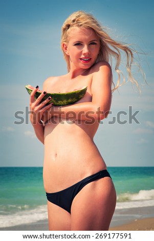 young beautiful girl, attractive blonde, enjoys tropical weather, eats a water-melon, wind develops beautiful long hair