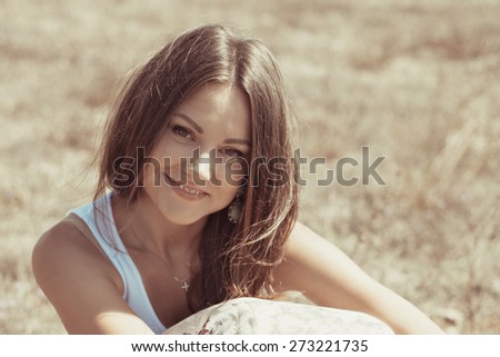 Portrait of beautiful young woman which sits on  grass on natural background. girl in a long skirt and with long hair poses in warm spring day