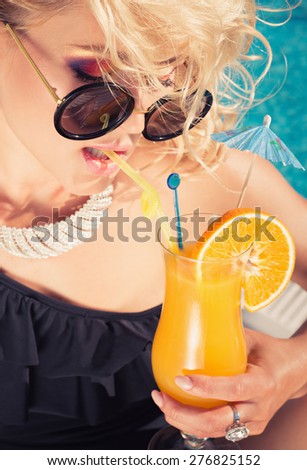 beautiful, suntanned, young sexy fashion woman drinking cocktail, and enjoys in the summer afternoon near the pool