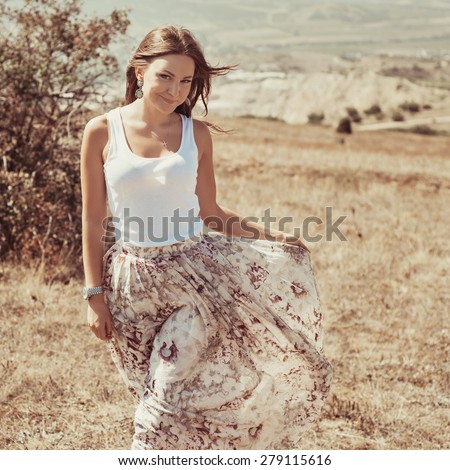 Portrait of the young beautiful smiling woman outdoors enjoying summer sun. wind in hair. girl in a long skirt and with long hair poses in warm spring day. Photo with instagram style filters
