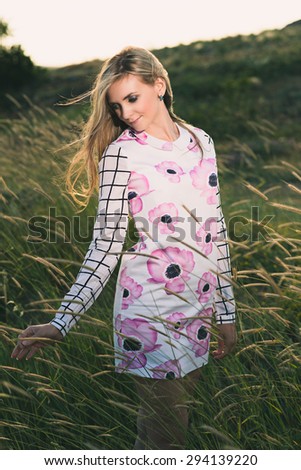 portrait of the attractive, slender, beautiful young Caucasian  blonde girl outdoor. Beautiful modern woman  with the long developing fair hair in a loose dress. dressy style. snub nose