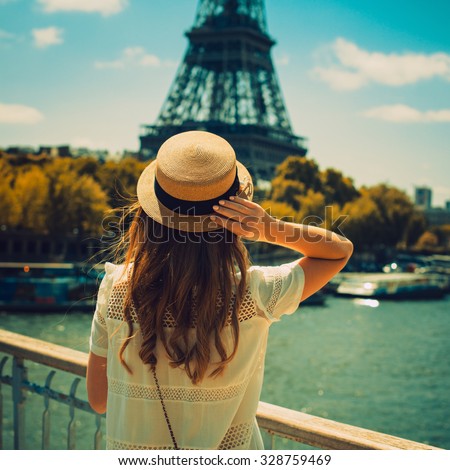 young attractive woman in hat, white dress, red bag poses in front of the Eiffel Tower in Paris. Photo with instagram style filters
