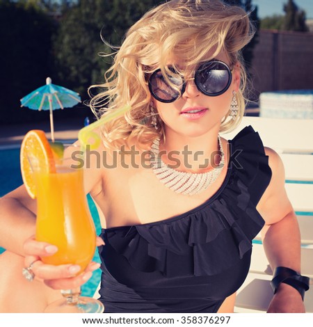 Fashion beautiful woman sunbathing on a chaise lounge with fresh orange juice in luxury pool. Photo with instagram style filters