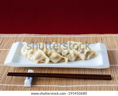 Gyoza or potstickers on a plate over a bamboo mat. Selective focus and deliberate shallow depth of field on background with copy space on top.
