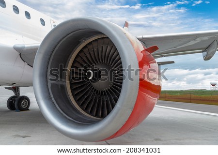 An airplane with focus on its red engine on the tarmac of an airport.