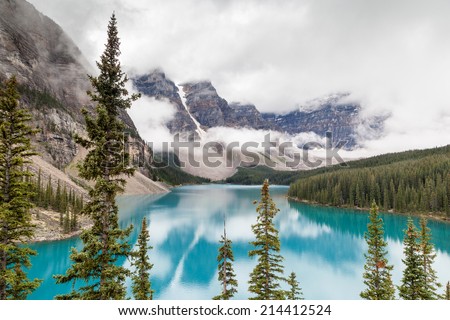 Fog and clouds descend onto the Valley of the Ten Peaks where glacier-fed Moraine Lake gives off its distinct turquoise color due to refraction of light off the rock flour at the bottom of the lake.