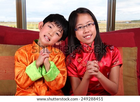 Two cute children in traditional Chinese New Year outfits making a Chinese-style greeting gesture.