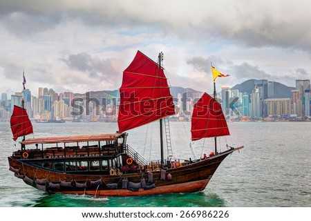 A typical Chinese junk ship on Victoria Harbor in Tsim Sha Tsui, Hong Kong. The emerald-colored seawater and low clouds near sunset created a colorful glow on the skyline in the background. HDR.