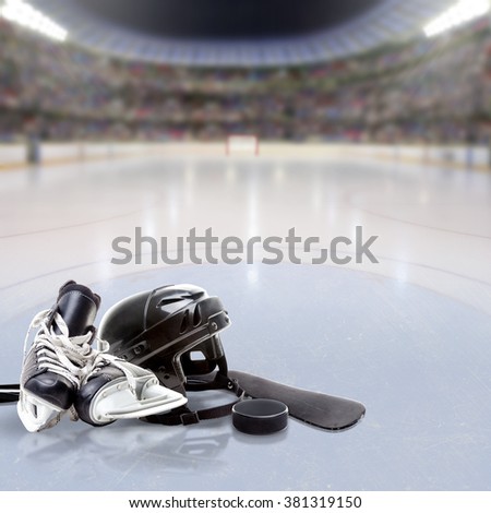 Dramatic Hockey arena full of fans in the stands with helmet, skates, stick and puck on reflective ice and copy space. Deliberate focus on equipment and shallow depth of field on background.
