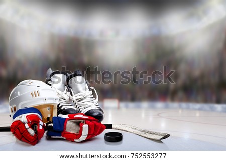 Low angle view of hockey helmet, skates; gloves; stick and puck on ice with deliberate shallow depth of field on brightly lit stadium background and copy space.