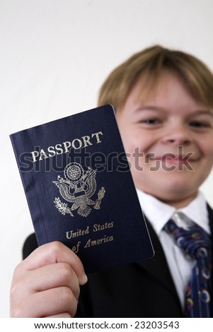 A young boy holding up a passport for inspection. Dressed in a business style suit to create a business theme, a child holds out his passport with focus on the id.