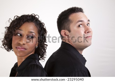 Woman looking over her shoulder at a man flashing an innocent look. Couple back to back.