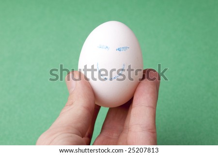 An egg decorated in blue crayon with a happy smiley face. Held forward in a hand