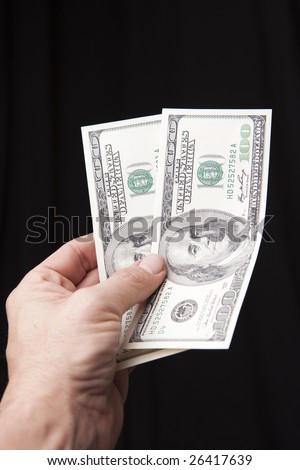 The hand of a person holding two one hundred dollar bills isolated on a black background