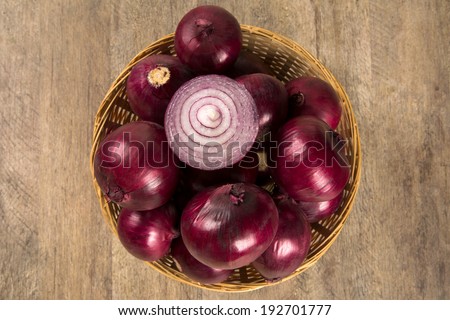 Red onions and a red onion cut in a half in a basket over a table seen from above.
