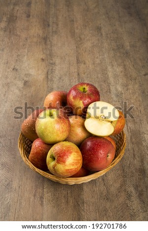 A basket full of apples and an apple in a half over a table.