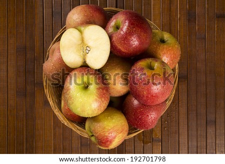 A basket full of apples and an apple in a half over a table seen from above.