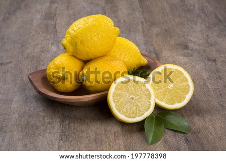 A lemon cut in a half in front of a pot of lemons over a wooden surface.