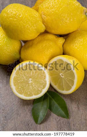 A close up of a lemon cut in a half in front of some lemons over a wooden table.