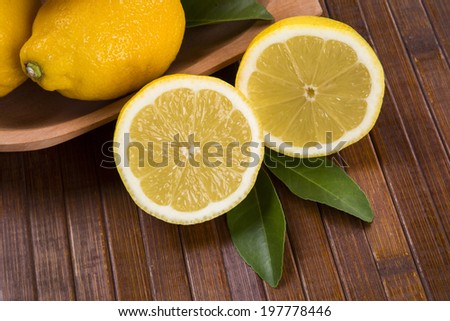 A close up of a lemon cut in a half in front of a pot of lemons over a wooden surface.