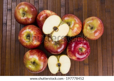 Some entire red apples and a red apple cut in a half over a wooden surface