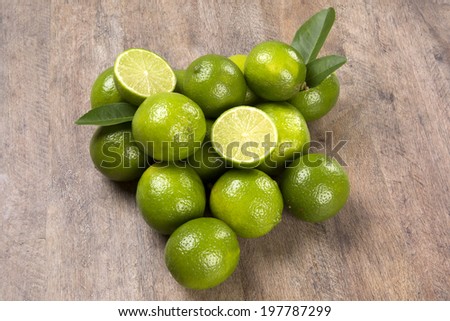 A lemon cut in a half above some entire lemons with leaves over a wooden surface.