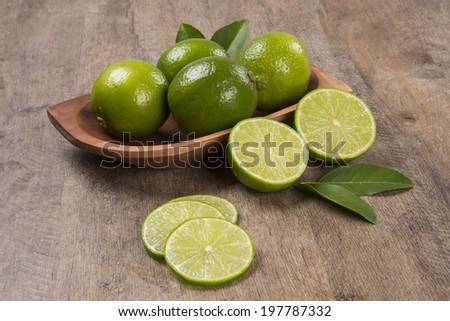 A lemon cut in a half and three slices of lemon in front of a pot with lemons over a wooden surface.