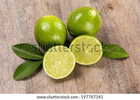 A lemon cut in a half in front of two entire lemons with leaves over a wooden surface.