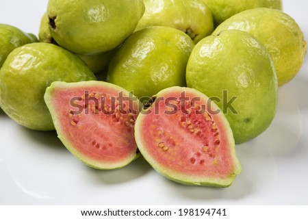 A close up of a brazilian guava cut in a half in front of some entire guavas.