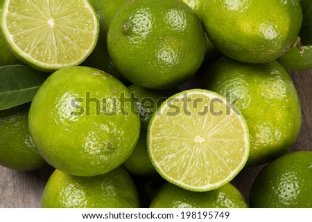A close up of a lemon cut in half above some entire lemons over a wooden surface.
