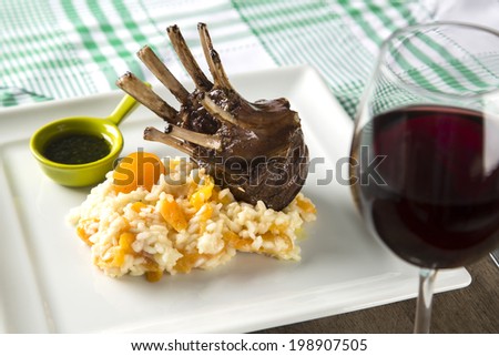 A delicious dish of Rack of Lamb with rice and apricot on a square plate with wine.