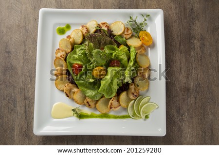 A dish of king scallop with potatoes and salad in a plate over a wooden surface seen from above
