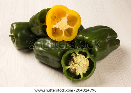 An yellow pepper cut in a half over some green peppers over a wooden surface