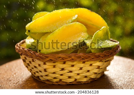 Some caramboles in a basket getting watered over a wooden surface on a green and natural background