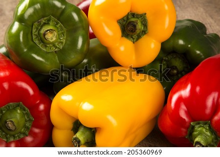 Close up of some red, green and yellow peppers over a wooden surface