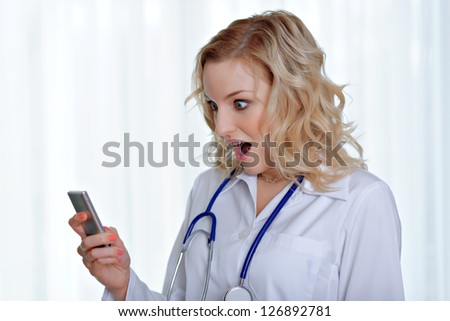 Surprised caucasian female doctor reading sms on mobile phone, standing