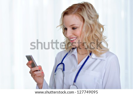 Attractive caucasian female doctor reading sms on mobile phone, standing