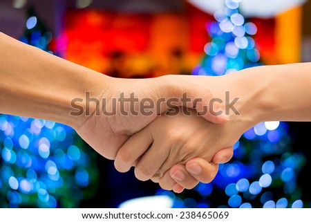 Business man and woman make hand shake with abstract bokeh christmas tree in shopping mall.
