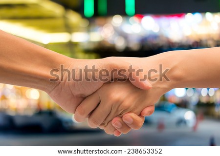 Business man and woman make hand shake with abstract bokeh light of shopping mall.