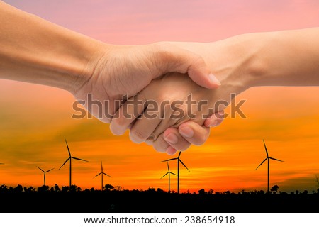 ConceptBusiness man and woman make hand shake with beautiful wind turbine generator farm during sunset.