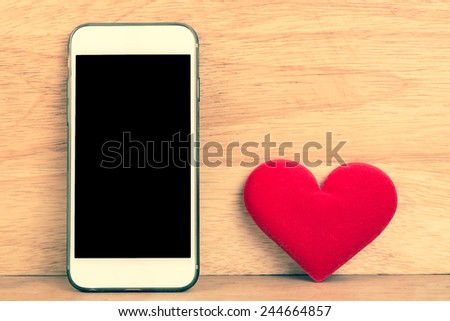 Smart mobile phone with red heart on wooden background. Retro filter.Valentines Day background.
