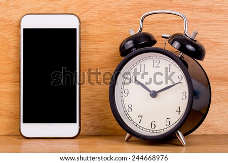Concept mobile smart phone and alarm clock on wood board background.