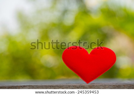 Red fabric heart on table with bokeh green leaf background. Valentines Day background.