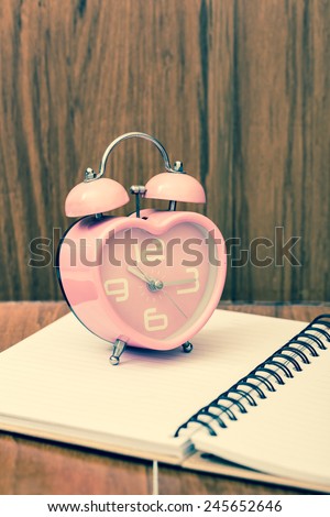 intage heart shape alarm clock  on open notebook. With wood background. Retro filter.