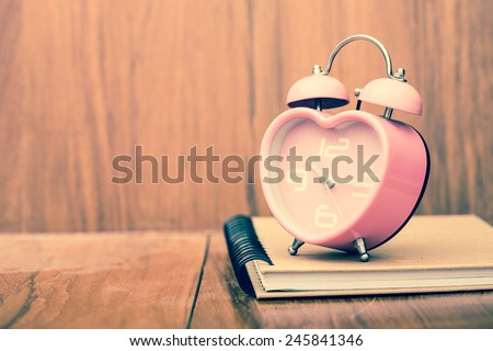 vintage heart shape alarm clock on notebook. With wood background. Retro filter.
