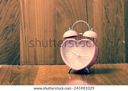 Vintage pink heart shape alarm clock on wood background. Retro filter.